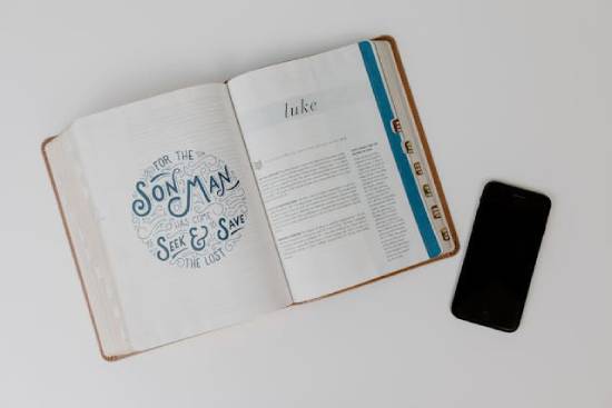 A phone with a Bible next to it that is open to the first page of Luke  A phone with a Bible next to it that is open to the first page of Luke