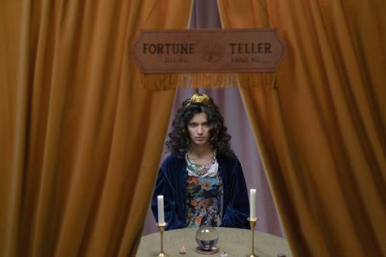 Woman with a Crystal Ball, Candles, and Sign above her that Reads "Fortune Teller" A woman sitting with a crystal ball and candles, depicting an example of fortune-telling.