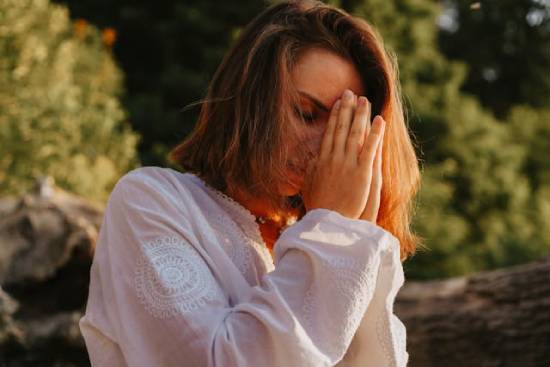 Woman Outside Praying to Overcome Demonic Spirits A woman prays with her hands folded and eyes closed, demonstrating how prayer can help overcome demonic powers.