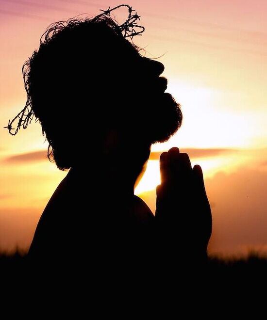 A silhouette of a depiction of Jesus praying and wearing a crown of thorns Jesus, wearing a crown of thorns, holds his hands up in prayer.