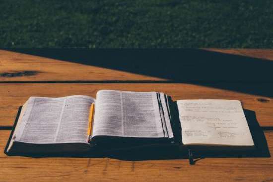 Open Bible with study notebook An open Bible and notebook lying on a wooden table.