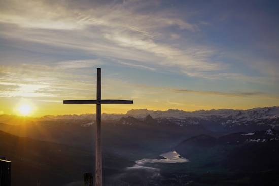 A cross stands by a river with a beautiful sunrise in the background