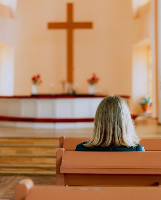 A woman sitting in a church pew stares up at a tall cross behind the pulpit. People sometimes do this when they think about what the Lord's Supper means for them.