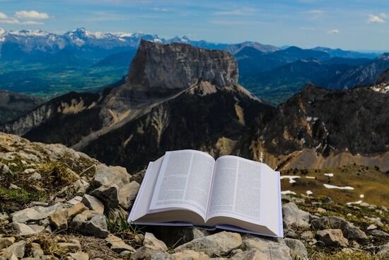 An open Bible on a rocky hillside facing the mountains.