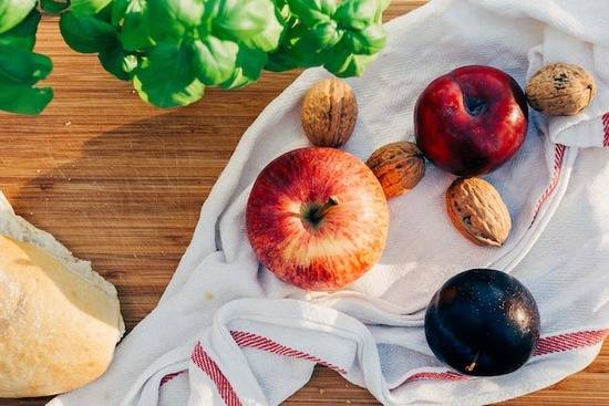 An assortment of plant foods on a cloth: apple, plum, nuts, bread, and basila meal after deciding to give up meat eating