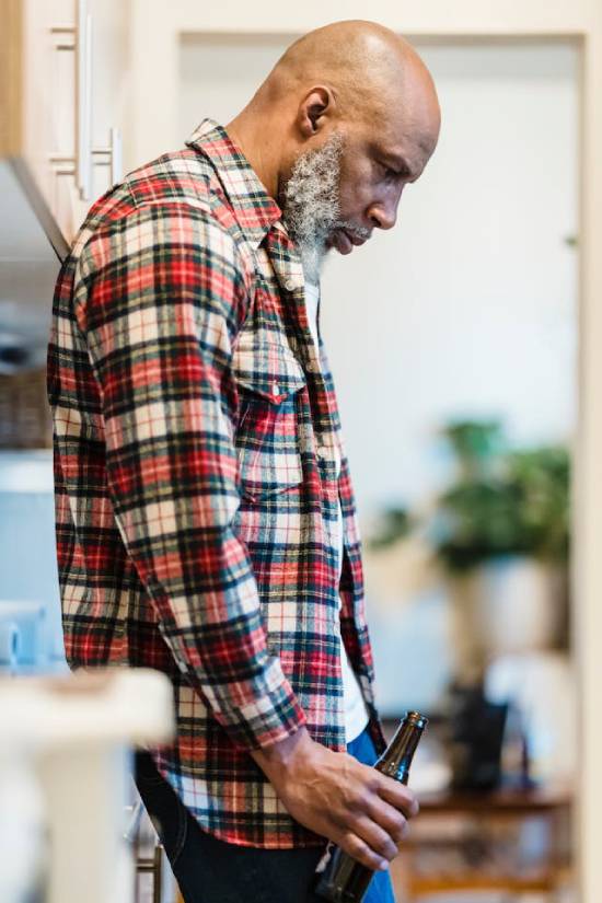 A man looks down at the ground with a despondent expression and a beer bottle in his hand. Shame is a feeling we often experience when we give in to our temptations.