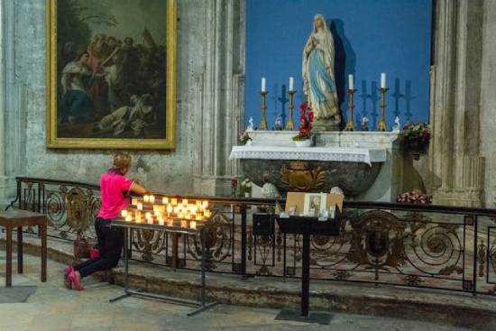 A woman kneels in prayer in front of candles and a statue of Mary, illustrating the third angel's warning against false worship. 