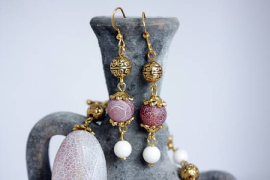 Dangling gold and red earrings hanging from the mouth of a clay jar Two ornate earrings hang on the lip of a clay jar.