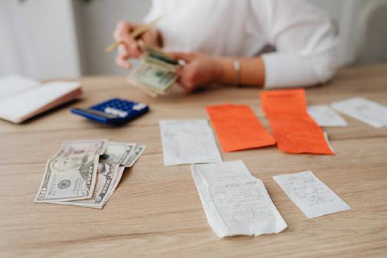 a person sitting at a table with a calculator and receipts laid out in front of them, counting money in their hand