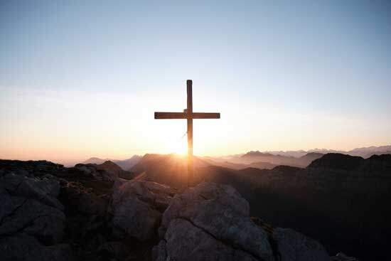 Cross at sunrise A wooden cross on a mountain with sunlight shining from behind it