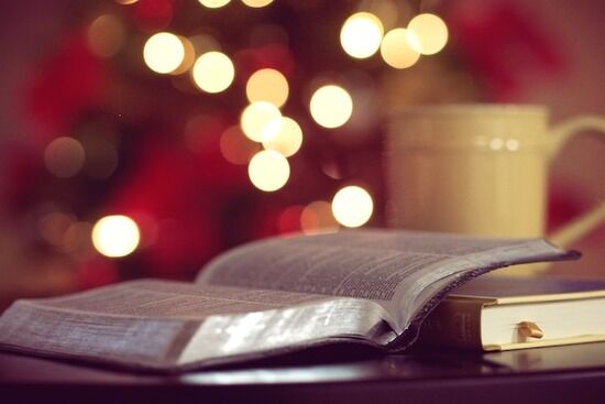 Open Bible on Table A Bible open with a Christmas tree lit in the background