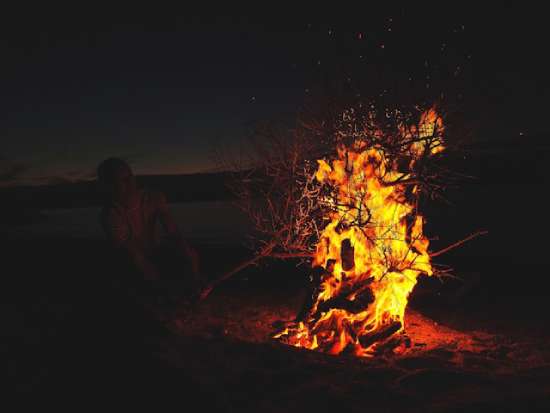 Burning Bush A person adding tree branches to a fire in the desert at night.