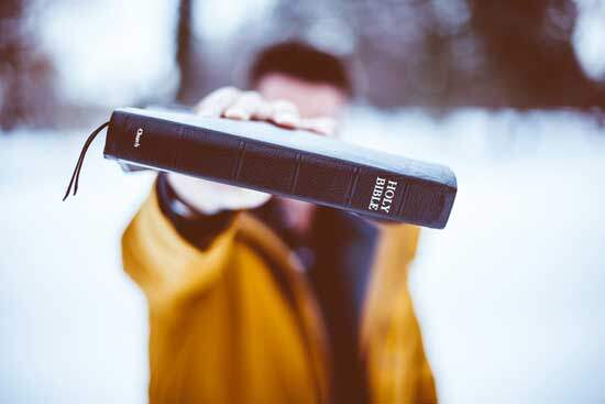 Man Holding Out Bible A man in a snowy forest holds out a copy of the Holy Bible.