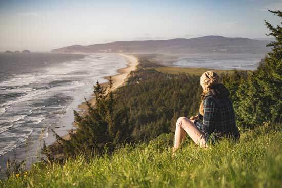 Woman spending time with God in nature A woman sitting on a grassy hillside that overlooks the ocean and spending time with God in nature