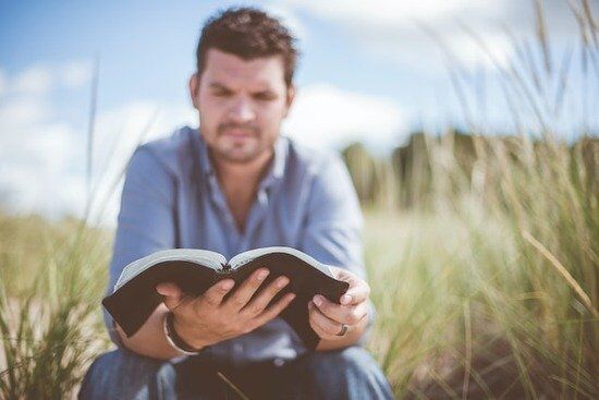 Man reading his Bible in a grassy field A man reading the Bible to gain strength from God against temptation