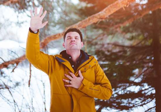 Man praying raise hand A man stands in a forest with his eyes closed and right hand raised up to show he's praying.