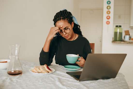 Woman eating at computer thinking about a difficult decision A woman eating breakfast by her computer as she ponders a difficult decision.