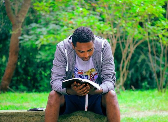 A man sits on an outdoor bench, reading a Bible