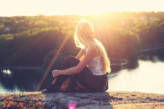A woman sitting by a lake and getting sun exposure