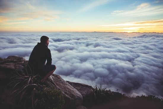 A man on top of a mountain overlooking a field of clouds, representing Moses on top of Mt. Sinai