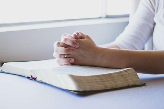 A person praying with their hands on an open Bible, showing how some people use Scripture to help them pray.