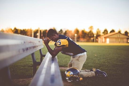 Football player praying A football player kneeling in prayer at a bench