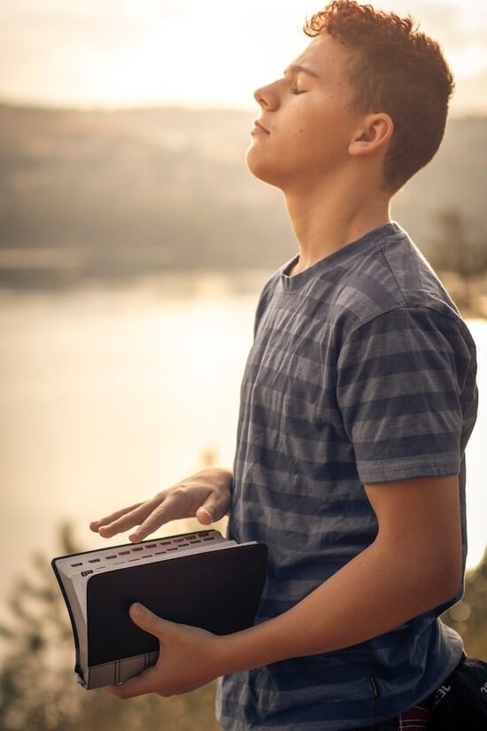 Young man holding Bible A young man holding a Bible and praying because he has peace through salvation in Jesus Christ