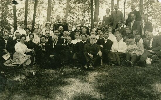 Ellen G. White with Australian workers, 1909. A black and white photo of Ellen G. White with a group of people in Australia. They are in a wooded area, most sitting in the grass and some standing.
