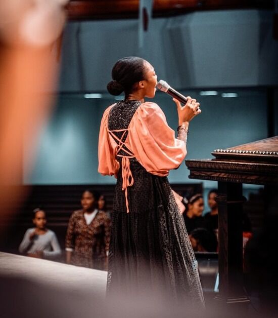 Woman singing A woman sings while people stand during church service. Praising God through music is one way we can have fellowship with others.