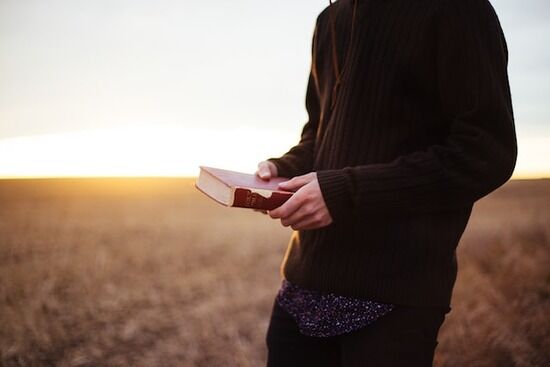 Outside with Bible A man holding a Bible while walking in a field at sunset