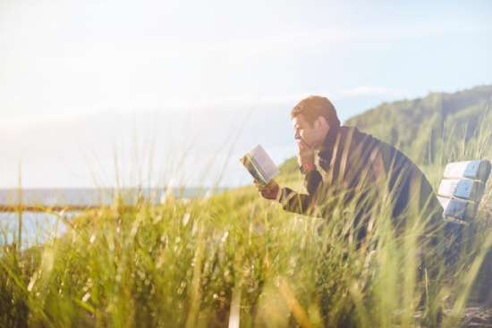 Man Contemplating Bible A man leaning forward and reading the Bible as he sits in a grassy field overlooking a lake