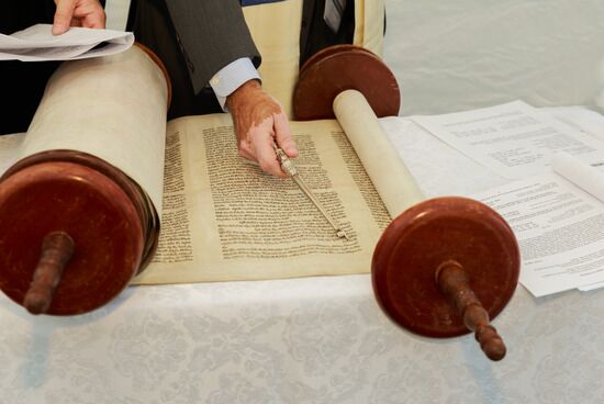 Two Men Studying Ancient Bible Scrolls A hand using a pointer to read ancient scrolls of the Bible