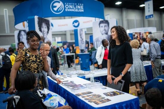 People talk at a booth in the exhibit hall, where attendees can learn about different Adventist ministries and projects.