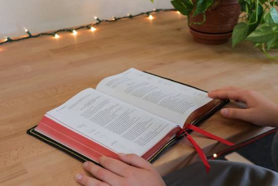 A person sits at a desk reading an open Bible