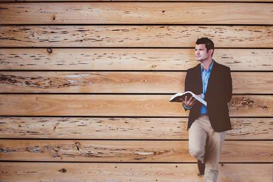 Man Leaning Against a Wall Reading Bible A man leaning against a wall reads his Bible, possibly thinking about what it says about God's appearance.