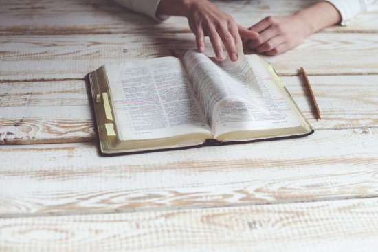 Person reading open Bible on table Hands turning through the pages of an open Bible