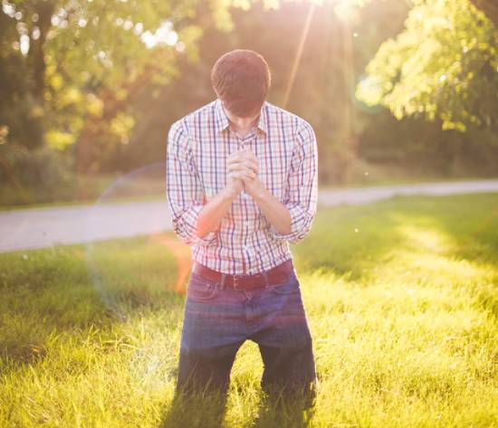 Man kneeling on grass praying A man kneeling in the grass while praying illustrates what it may look like for someone to accept Christ's gift of salvation.