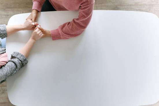 Two people sitting at a white table, holding hands and showing a caring relationship.