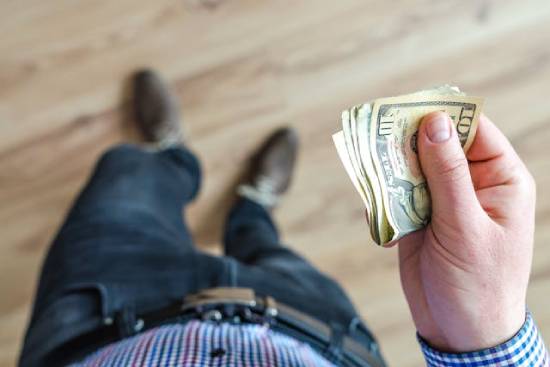 A hand places a folded $1 bill into a cross-shaped slot, signifying that a small portion of our income should be dedicated to God, as He provided the ultimate sacrifice for us.