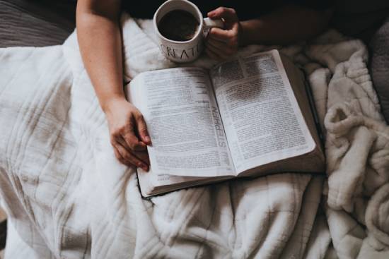 Person holding a cup of tea while reading the Bible