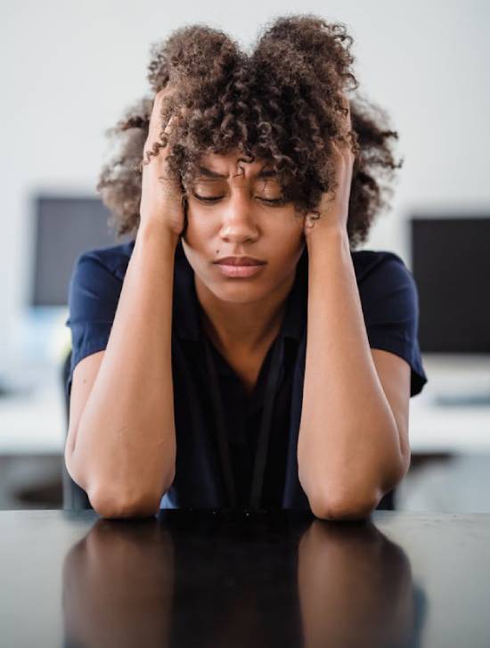 Burnt out woman with her head in her hands A woman sitting at a desk with her hands on her head, illustrating the signs of frustration and burnout.