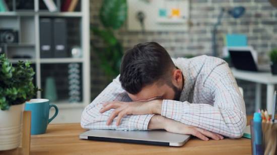 Man with his head on his desk feeling overwhelmed A man with his head down on a desk, illustrating the feeling of overwhelm.