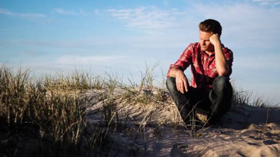 A Man Sitting Outdoors Feeling Doubtful A man sits on the beach while lost in his thoughts, showing how doubt can make us wrestle with our minds.