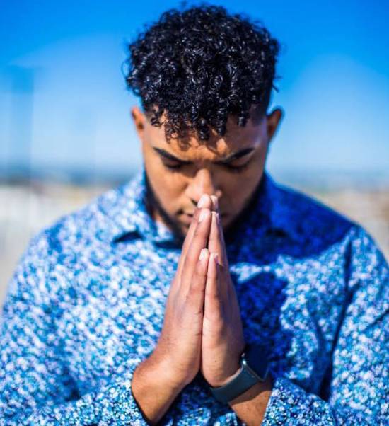 Man in a blue dress shirt praying A young man bows his head in reverent prayer.