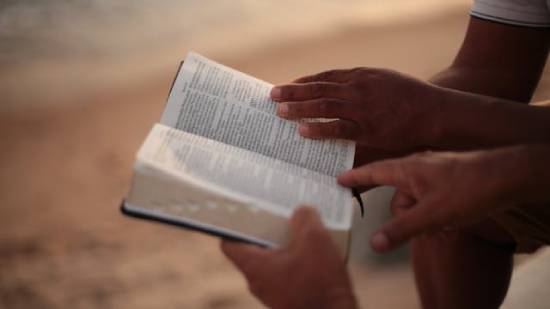 Two people reading a Bible on a beach. Two people reading a Bible on a beach.