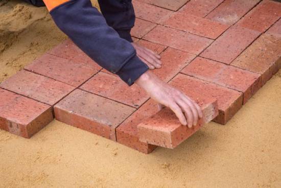 A person carefully lays down bricks on top of sand.