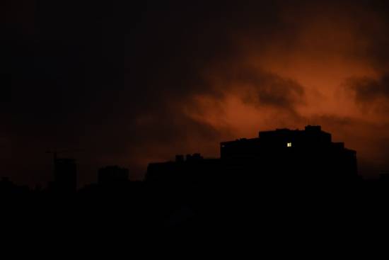Silhouette of a building against an orange and black sky A home in the distance against a dark, ominous sky shows one lit window.