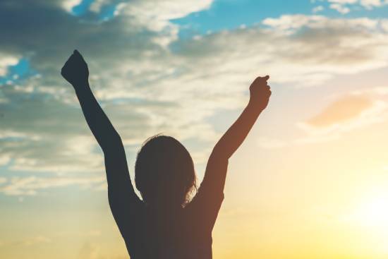 Silhouette of a girl raising her arms because she is encouraged by Jesus's words A silhouette of a young woman facing a sunrise with her arms raised in victory.