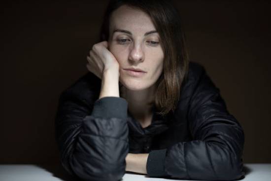 Woman looking sad who is going through personal challenges A young woman props up her head on a table and sadly stares in front of her.