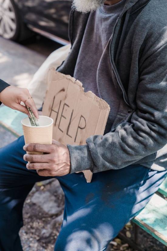 Woman putting money into a cup held by a homeless man Someone giving money to a person holding a sign that says